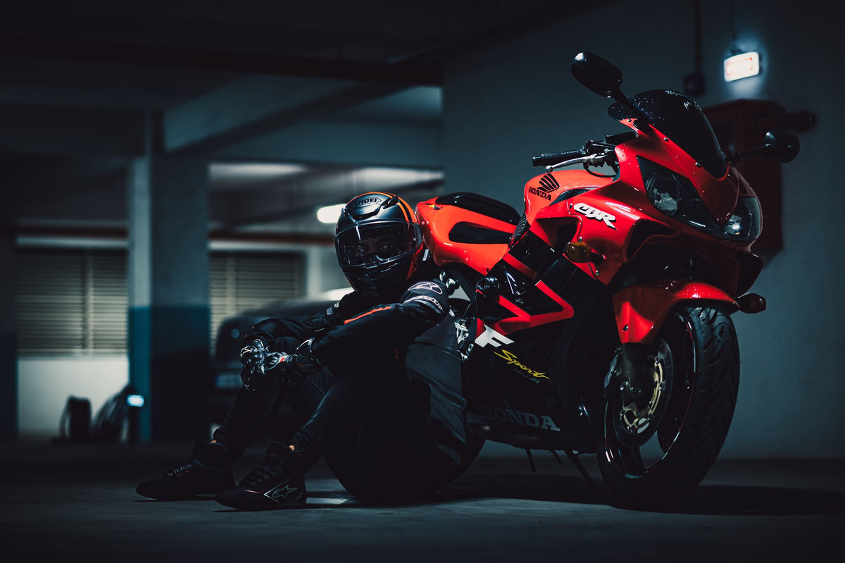 Red Honda sportbike with full fairings and a helmeted rider in a dark garage