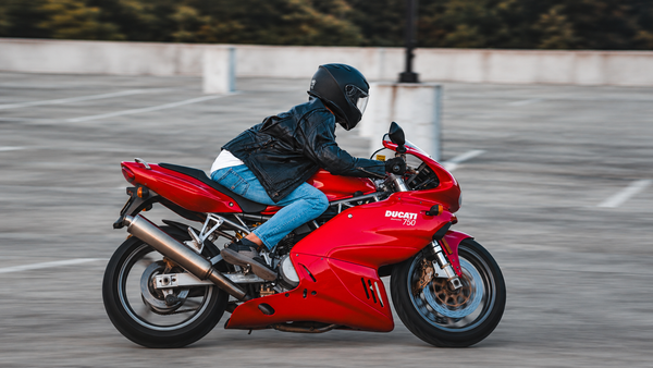 Rider wearing a black leather jacket, jeans and shoes on a red fully faired Ducati motorcycle, showing common gear-to-bodywork contact zones