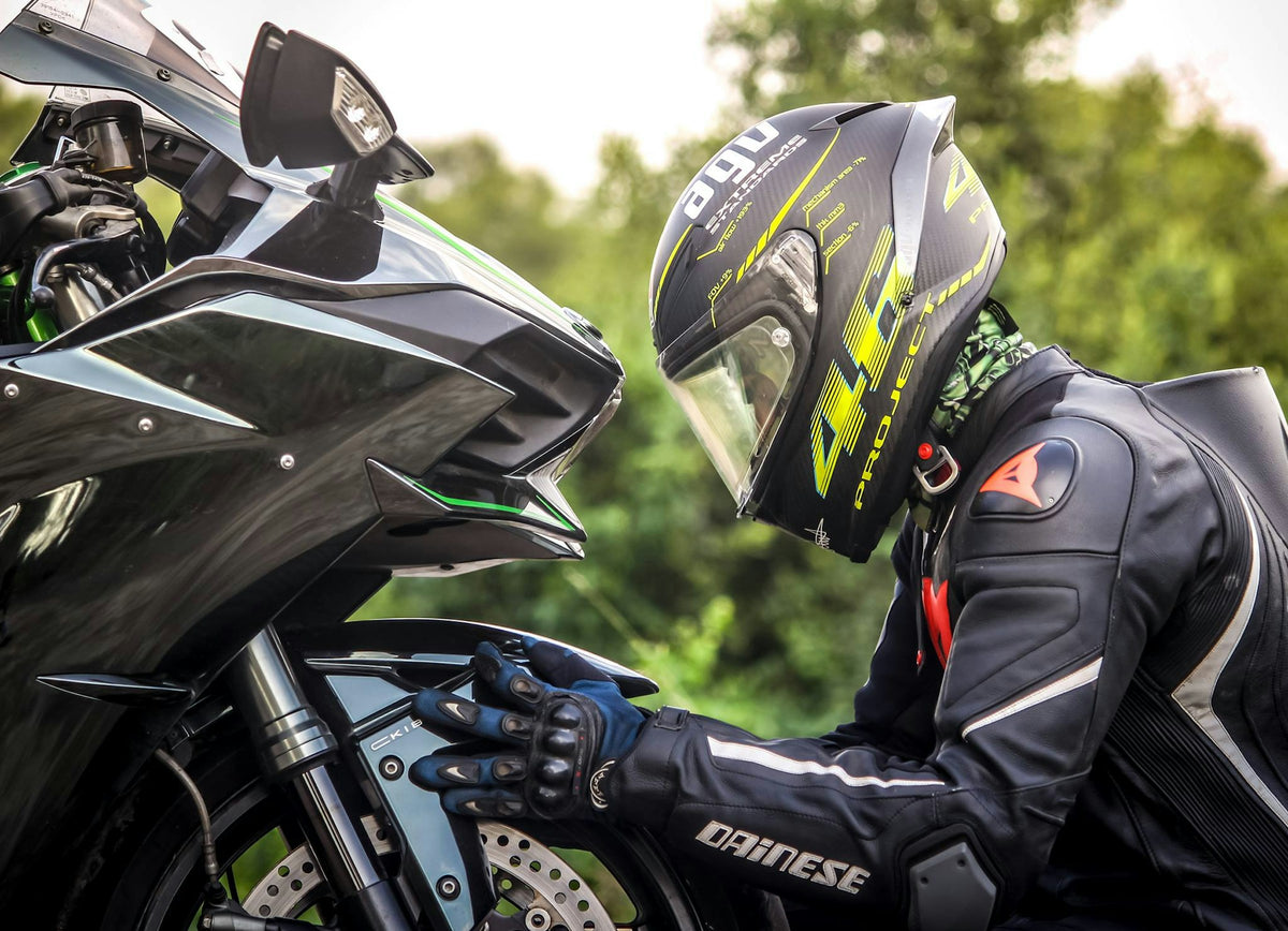 Motorcyclist in protective gear inspecting the front fairing and wheel area of a black Kawasaki sport motorcycle outdoors