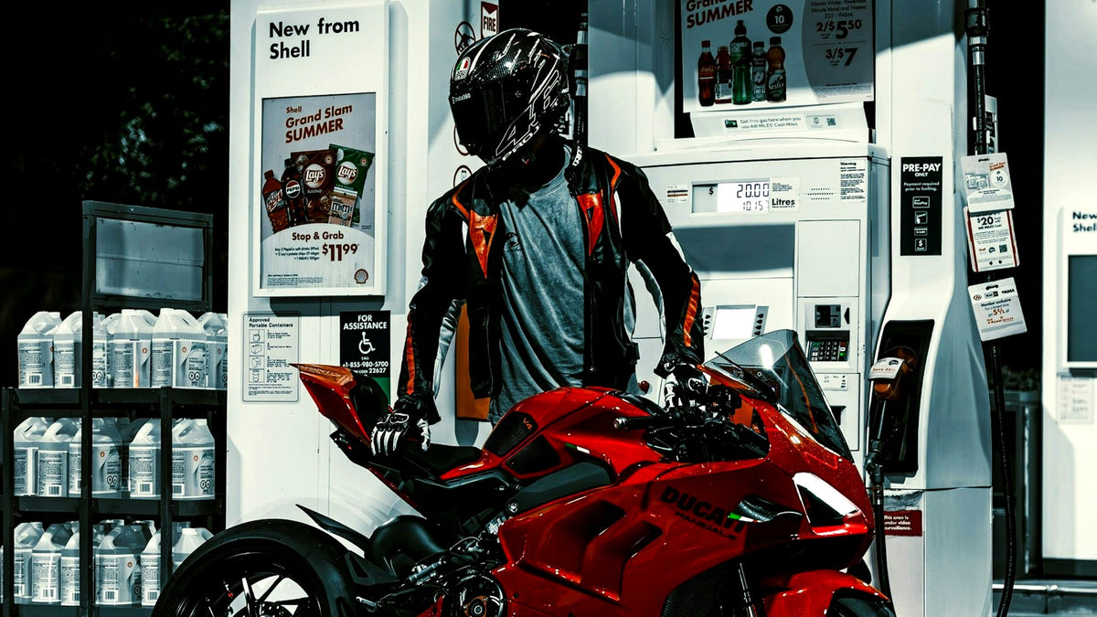 Helmeted rider refueling a red Ducati sportbike at a gas station at night