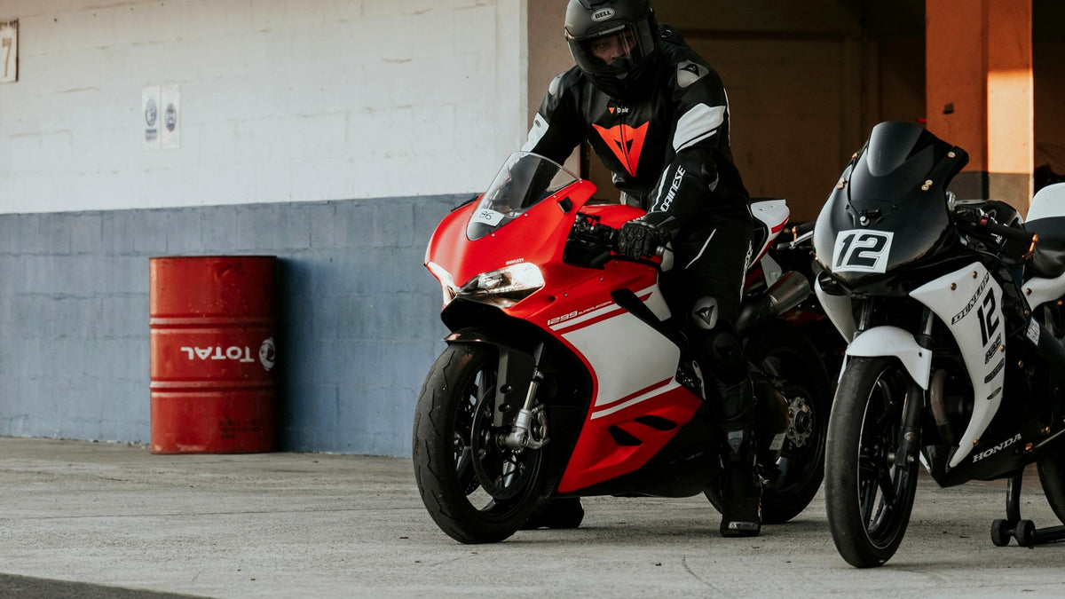 Helmeted track rider on a fully faired red sportbike in the pit garage before returning to the circuit