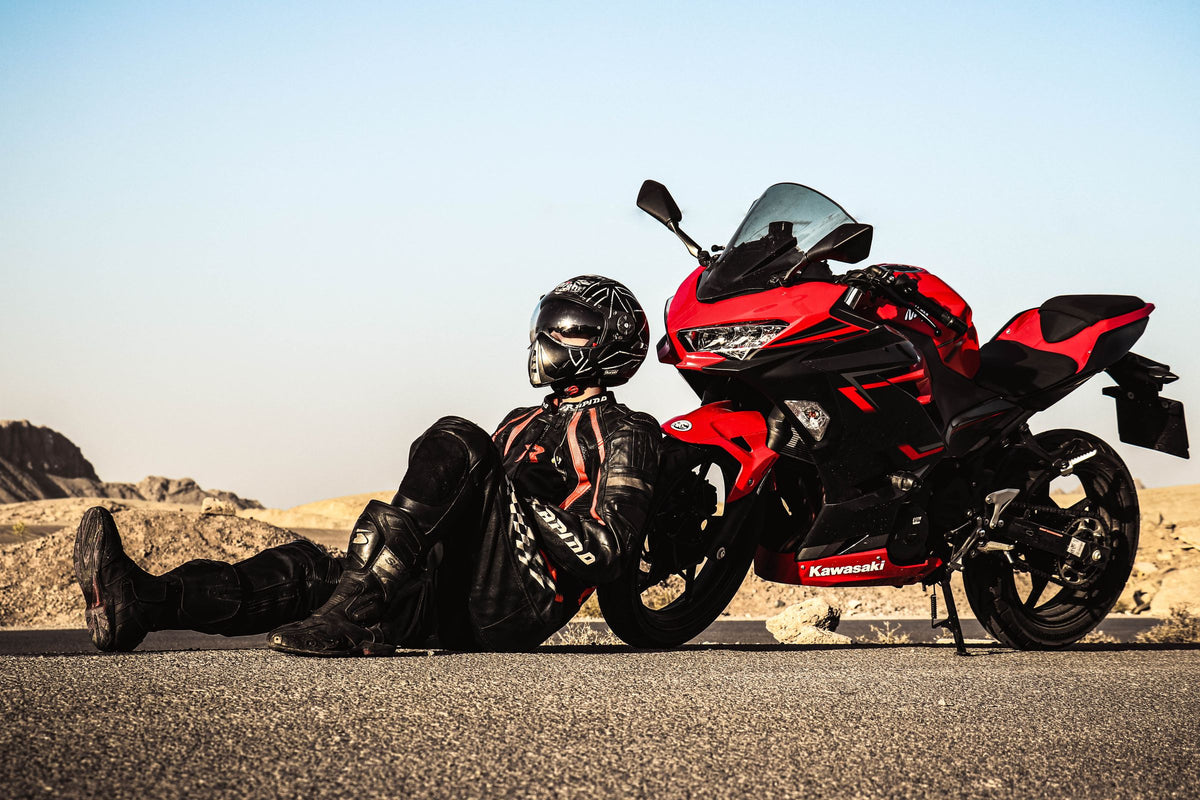 Helmeted rider resting beside a complete red sportbike on a desert road