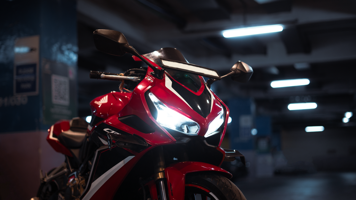 Red sportbike with glossy fairings black low-reflection panels and illuminated headlights in a dark garage