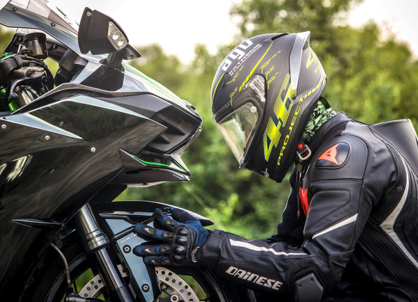 Motorcyclist in protective gear inspecting the front fairing and wheel area of a black Kawasaki sport motorcycle outdoors